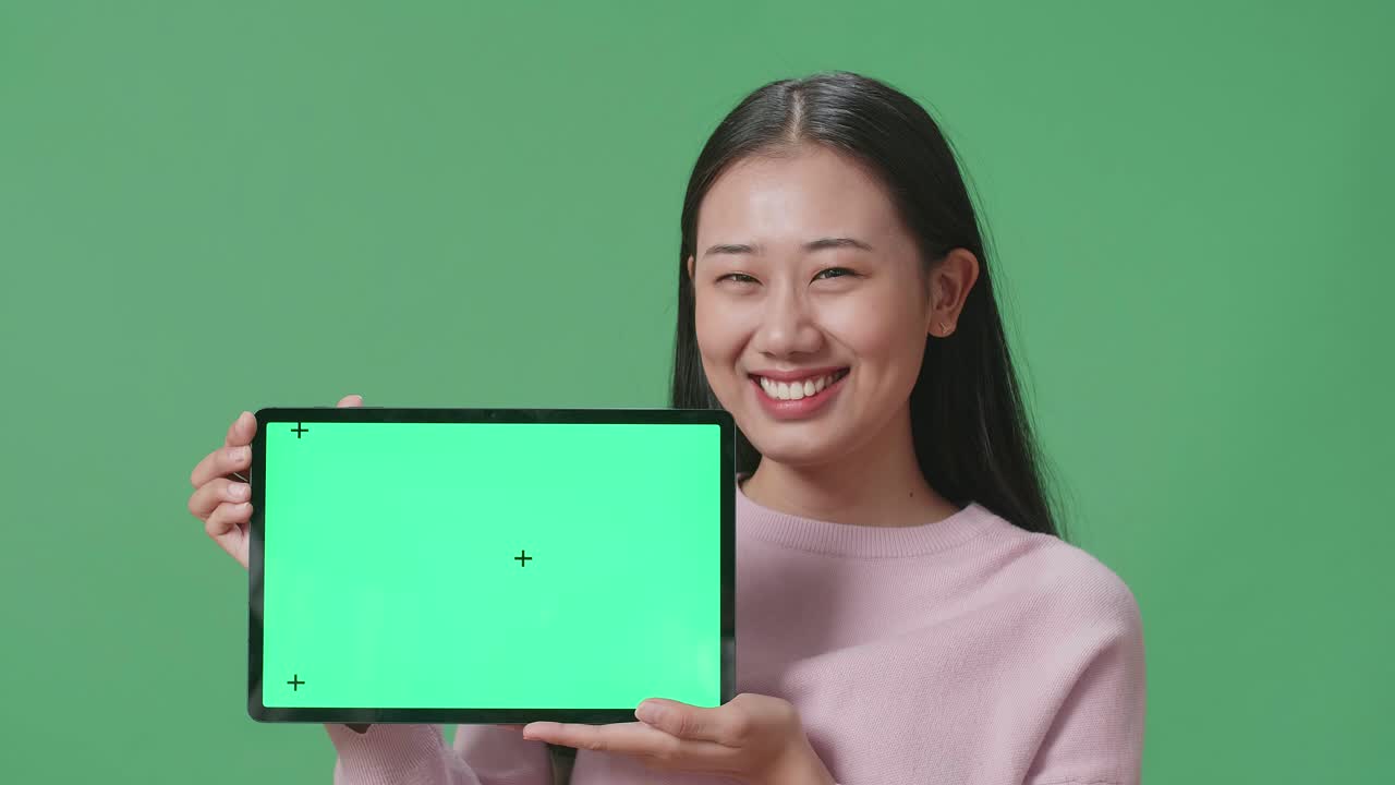 아시아 여성 학생이 녹색 스크린 스튜디오에서 태블릿 녹색 화면 모형을 보여주고 있습니다.