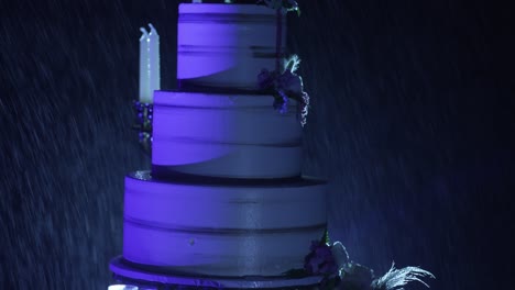 Dramatic-wedding-cake-with-purple-lighting-and-floral-accents-in-a-nighttime-setting