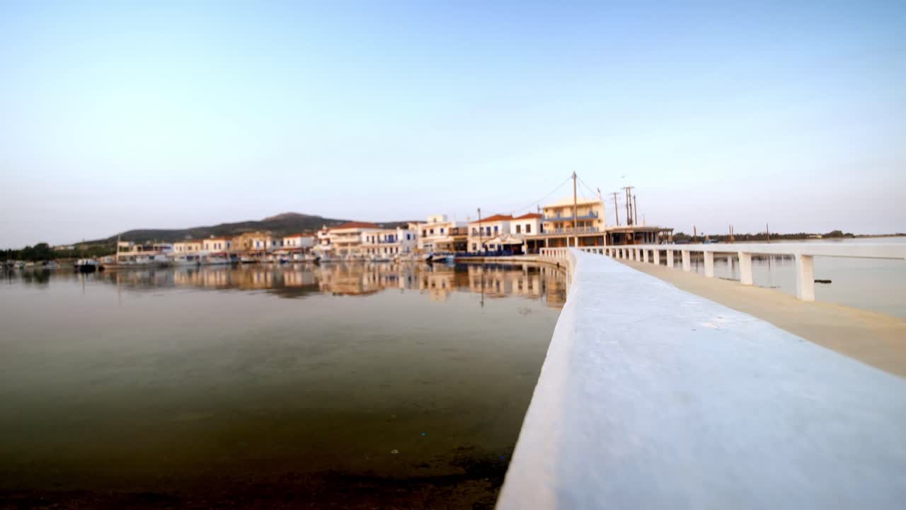 View of the white bridge and the coastal town of Elafonisos, Greece, at sunrise. Traditional architecture and calm sea reflections in a peaceful Mediterranean morning landscape