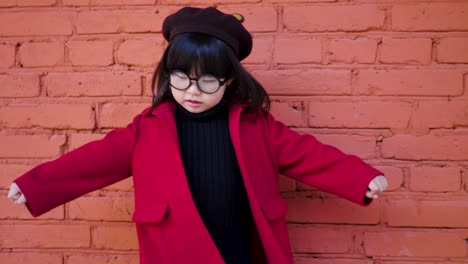 korean girl in a red coat and cap and round glasses dance on red brick wall the street in autumn