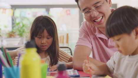 asian father having fun with children doing craft on table at home