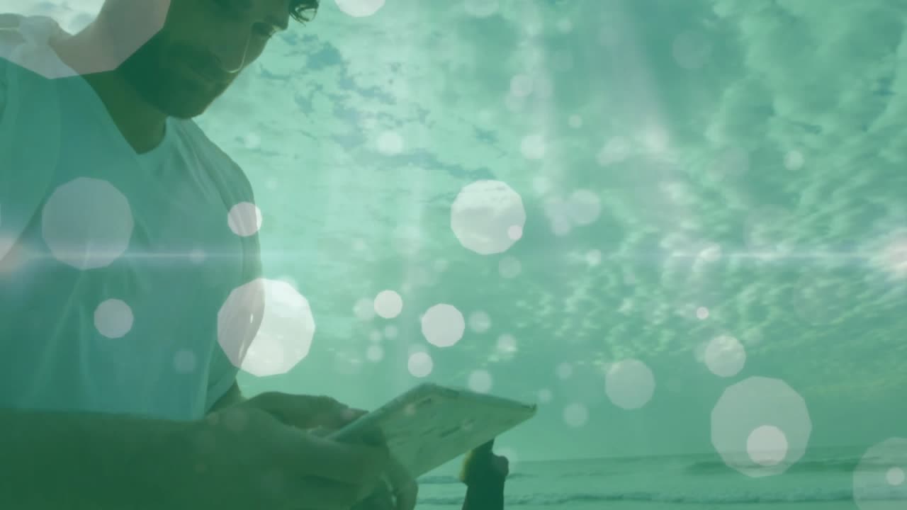 Uomo che digita sullo smartphone, inviando messaggi usando la tecnologia in spiaggia, con un overlay di bokeh verde crescente e una donna che osserva il mare.