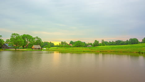 Zeitraffer-Eines-Wolkigen-Sonnenaufgangs-An-Einem-See-Mit-Hütten-Im-Hintergrund