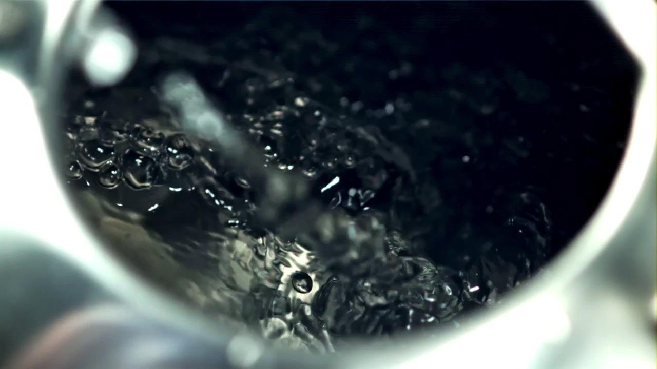 Primo piano di acqua che si versa in un contenitore scuro, creando bolle