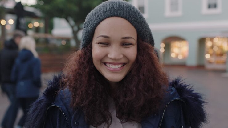 ritratto di una bella giovane donna con i capelli crespi sorridendo eccitata godendo di una serata urbana indossando un cappello di pelliccia