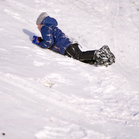 child boy having fun, rolls head over hills. playing and laughing on snowy winter walk in nature. frost winter season.cute little boy with having fun outdoors on winter day. ride down a hill, winter games and fun