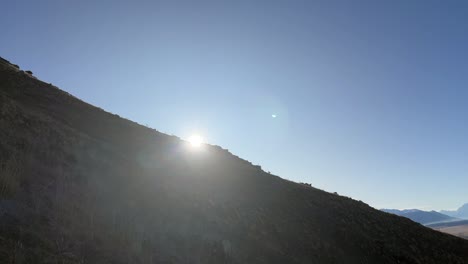 sun peeking from behind steep, grassy slope during sunset in the mountains