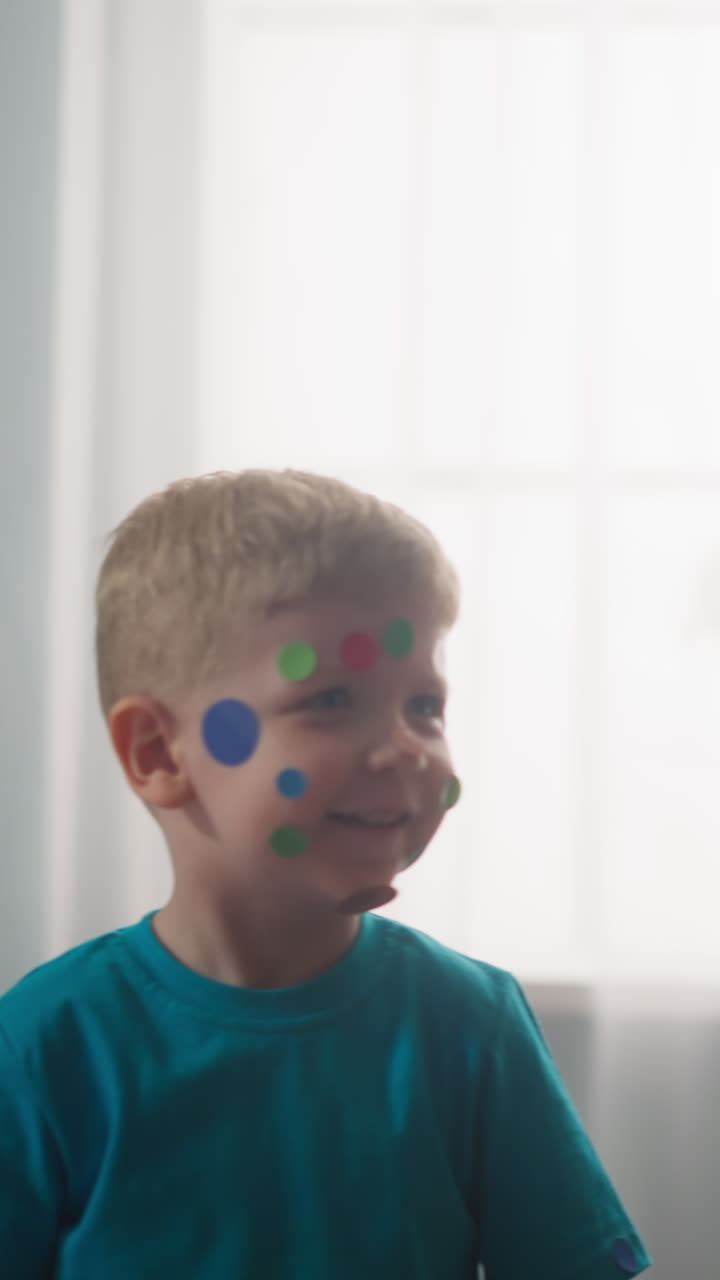 little children with colorful stickers on their faces, express joy, boy and girl play with stickers, look at camera and laugh