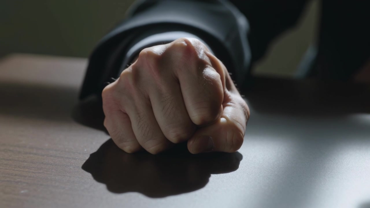 Pressing right fist on conference table after objection, suit sleeve and white cuff showing force