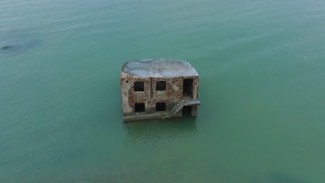 aerial birdseye view of abandoned seaside fortification building at karosta northern forts on the beach of baltic sea , waves splash, overcast day, rotating drone shot