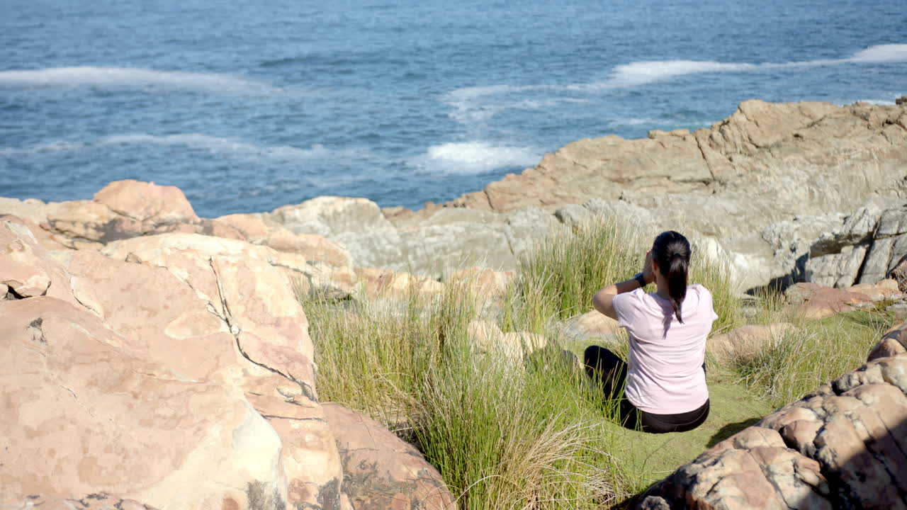 Sitting on rocky cliff, woman enjoying ocean view during mountain hike, copy space