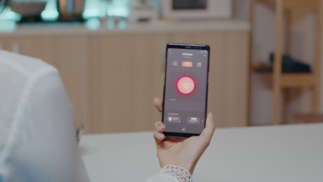 Woman-sitting-in-house-with-automation-light-system-holding-smartphone