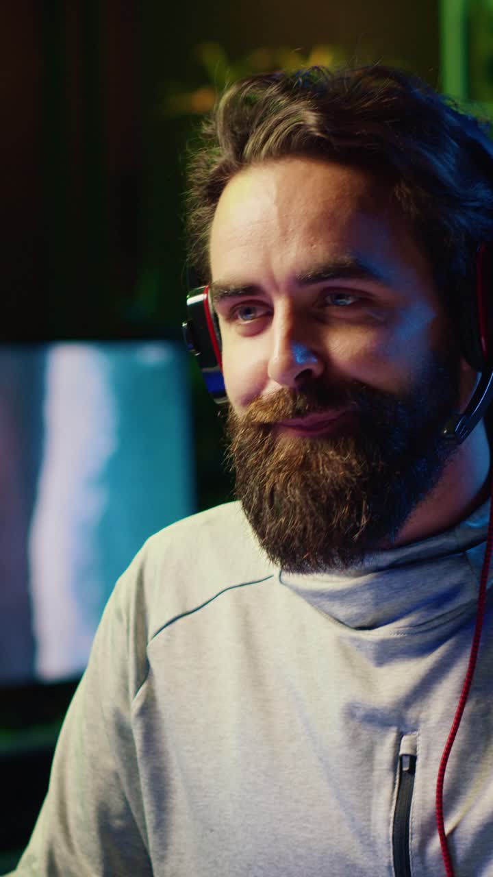 Video verticale di un felice giocatore professionista che trasmette in streaming una partita mentre parla con gli iscritti usando cuffie e microfono