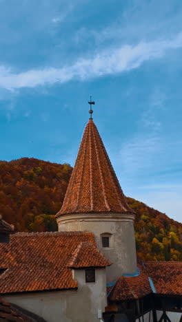 rooftops of bran castle in transylvania, romania. colorful autumn nature and blue sky at backdrop. vertical video