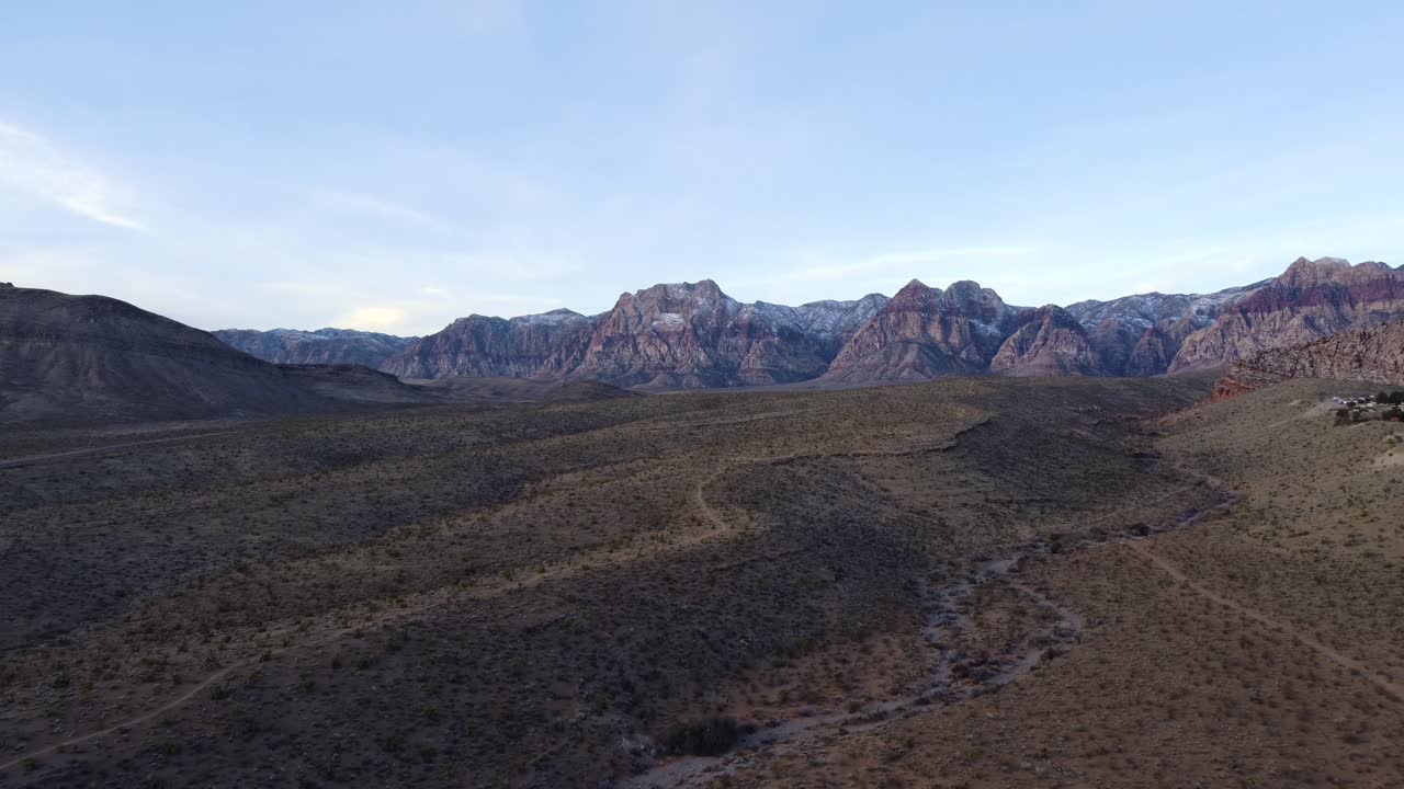 toma aérea del paisaje desértico y un lecho de río seco con las montañas de roca roja que contrastan con el paisaje a lo lejos