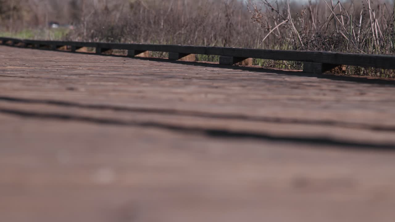 ground-level still shot focusing on a pair of black leather boots as they walk across a weathered wooden boardwalk