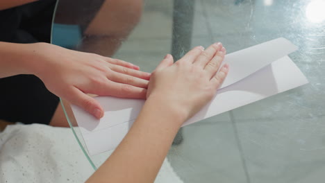 close-up of hands folding white paper carefully on the table, trying to create a craft project, with focus on detailed paper folding process during crafting activity