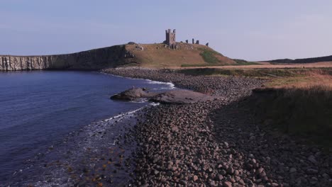 slow motion drone shot flying along the coastline towards dunstanburgh castle, northumberland, uk