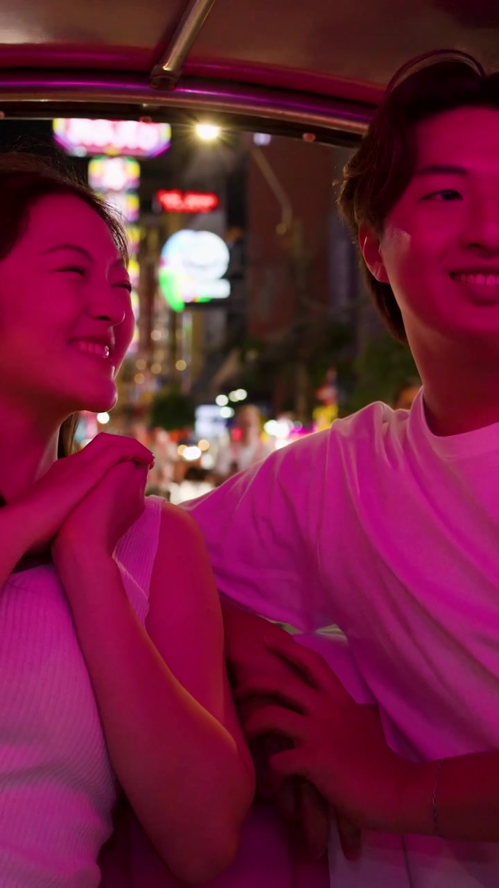 Una giovane coppia sorridente condivide un momento giocoso all'interno di un veicolo sotto una vivace illuminazione magenta.