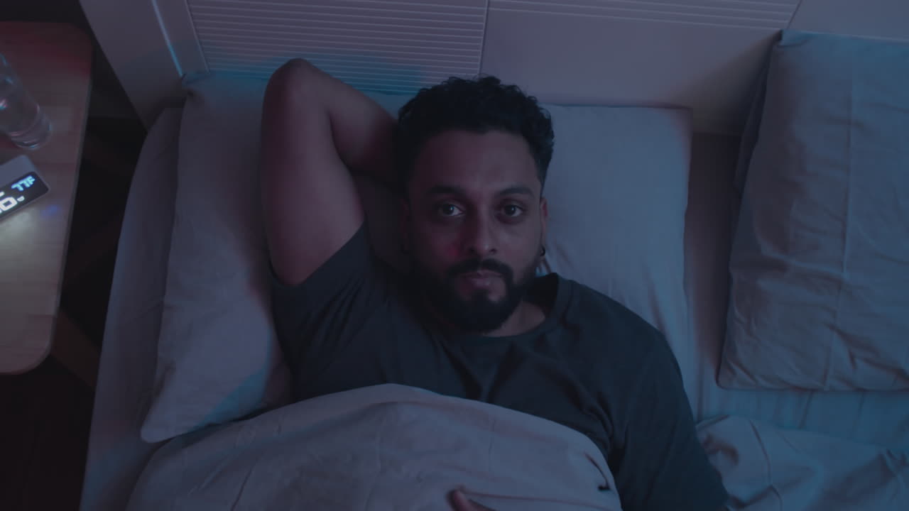 Sleepless Man Lying in Bed at Night and Looking at Camera