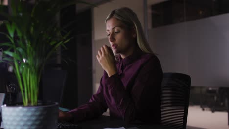 Video-of-tired-caucasian-businesswoman-sitting-at-desk-working-at-night-in-office