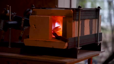 piece of metal being heated and worked in a home made forge, with the blacksmith's hand coming into view as he moves the piece around.