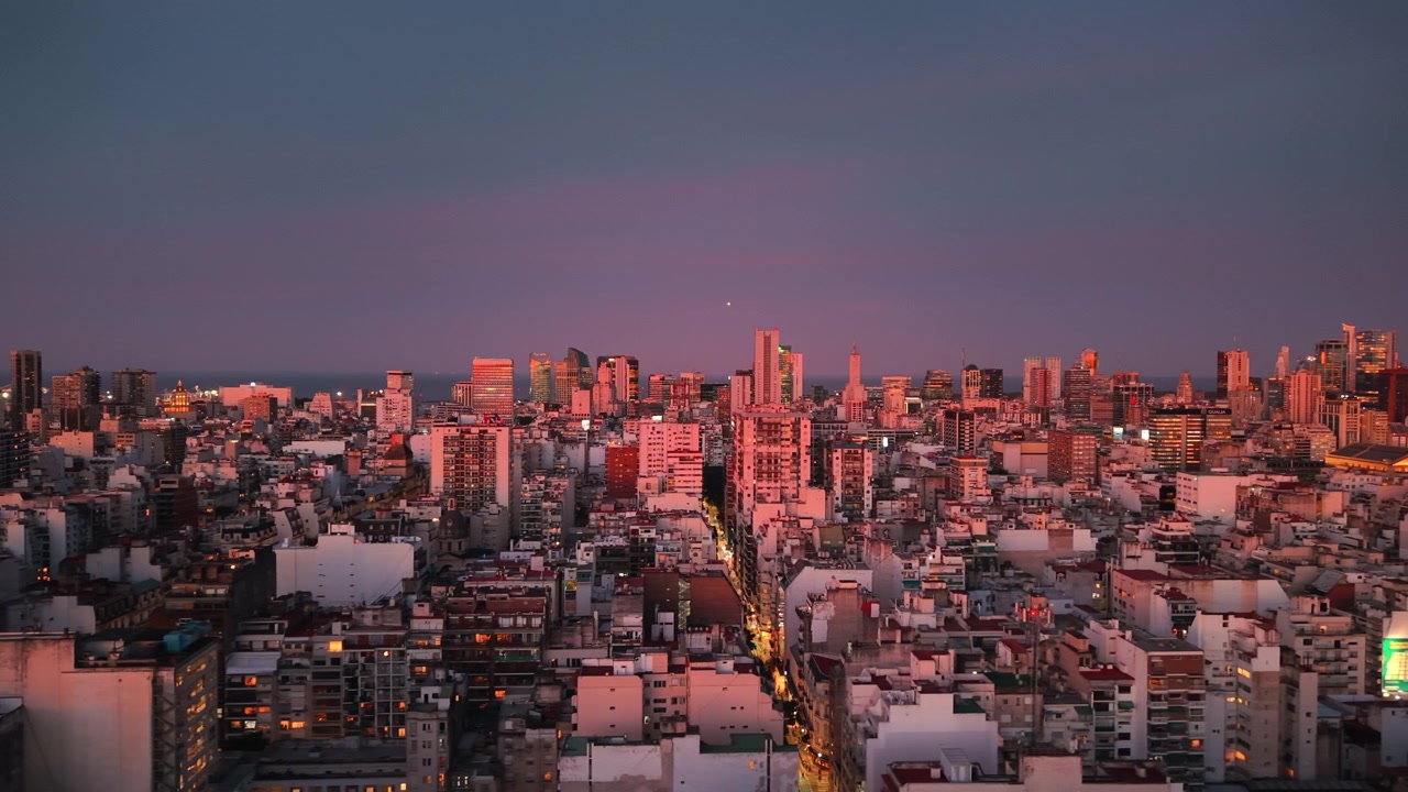 紺碧と紫色の澄んだ空の下、黄金色に輝く夕焼けに照らされ、光線が建物のファサードに当たる都市のビル群。