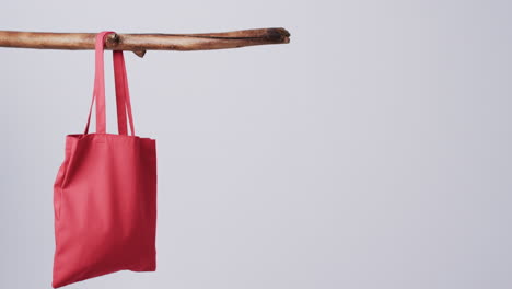 a red tote bag hangs from a wooden stick against a plain background, with copy space