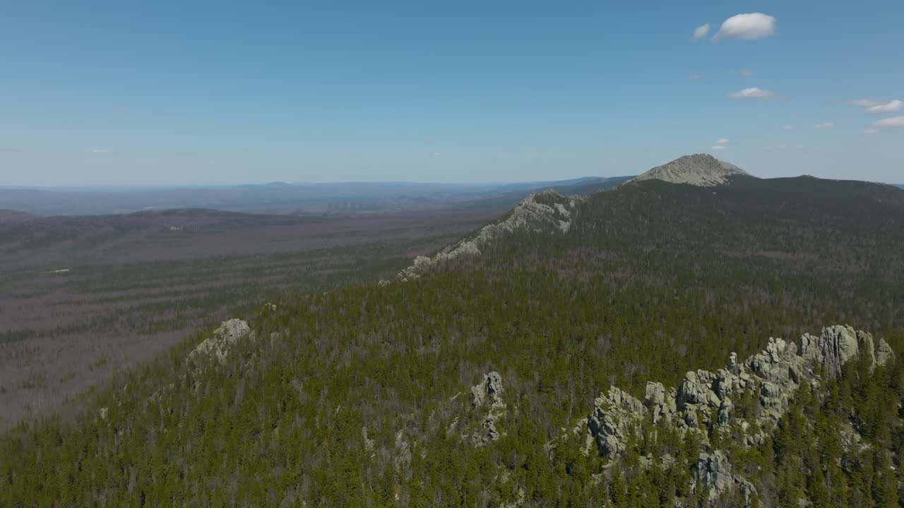 Droneoptagelser af klippefyldt bjergryg og stor taigaskov under blå himmel i Taganay Nationalpark, Tjeljabinsk oblast, Rusland, panoramisk vildmarkslandskab