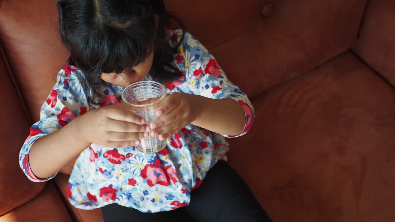 Little girl drinking water on the couch