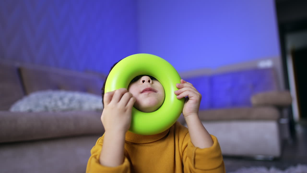 Caucasian toddler holding green ring from pyramid near his face. Baby boy showing his tongue funnily. Close up.
