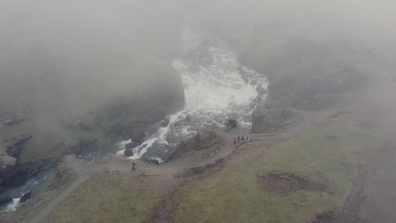 아이슬란드의 아름다운 폭포와 산책객들의 기분 좋지 않은 공중 드론 은 어두운 안개의 날에 모스 녹색 절벽과 바위 앞에 있습니다.