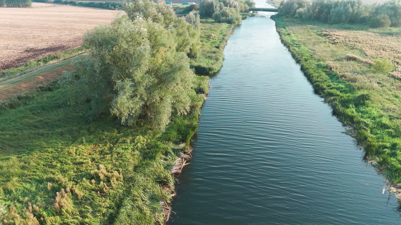 Aerial shot of a serene Great River Ouse flanked by lush greenery and agricultural fields, with trees and bushes along the riverbank under a partly cloudy sky.