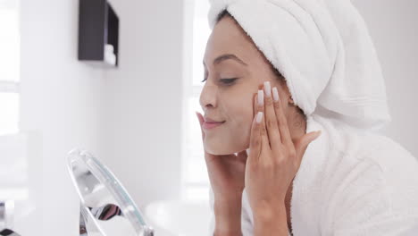 Biracial-woman-applying-face-cream-looking-in-mirror-in-bathroom,-slow-motion