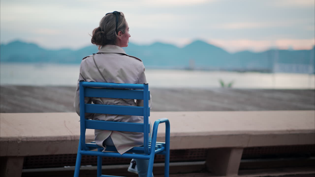 Woman in a trench coat sitting on a chair at the beach in France
