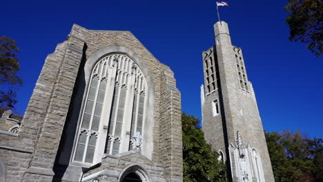 Camera tilts up from entrance of Gothic style church to bell tower with flag.