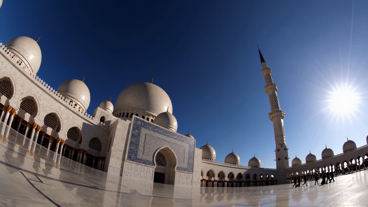 Un obiettivo fisheye cattura una vista dal basso di un grande cortile di moschea sotto un cielo azzurro limpido.