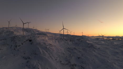 Spinning-wind-turbines-against-vivid-sunset-sky-atop-snowy-mountain,-Kvaloya