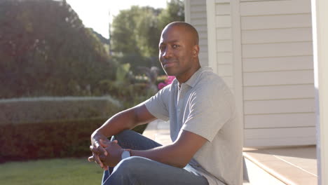 smiling african american man sitting on porch steps, enjoying sunny day at home