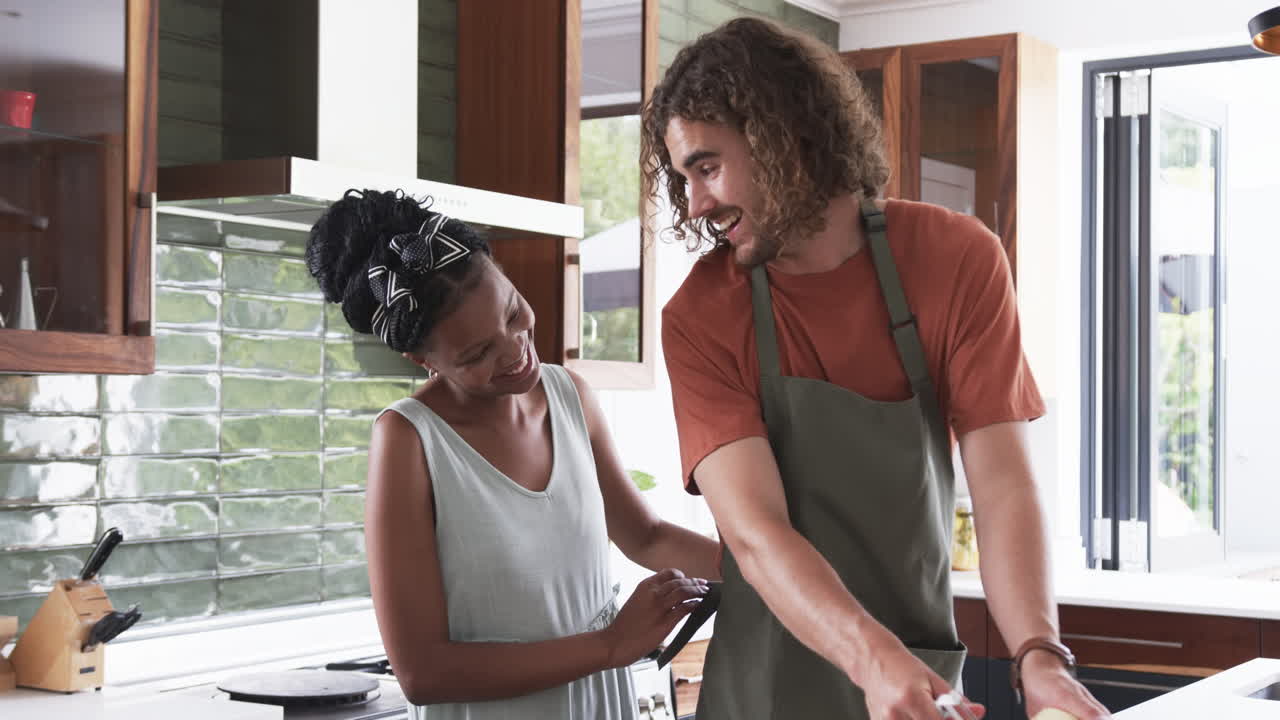 Diverse couple, a young African American woman and Caucasian man, cooking together at home