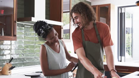 una pareja diversa, una joven afroamericana y un hombre caucásico, cocinando juntos en casa.