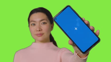 녹색 스크린 4에 대항하여 카메라를 향해 파란 화면 휴대전화를 들고 있는 웃는 여성의 스튜디오 초상화