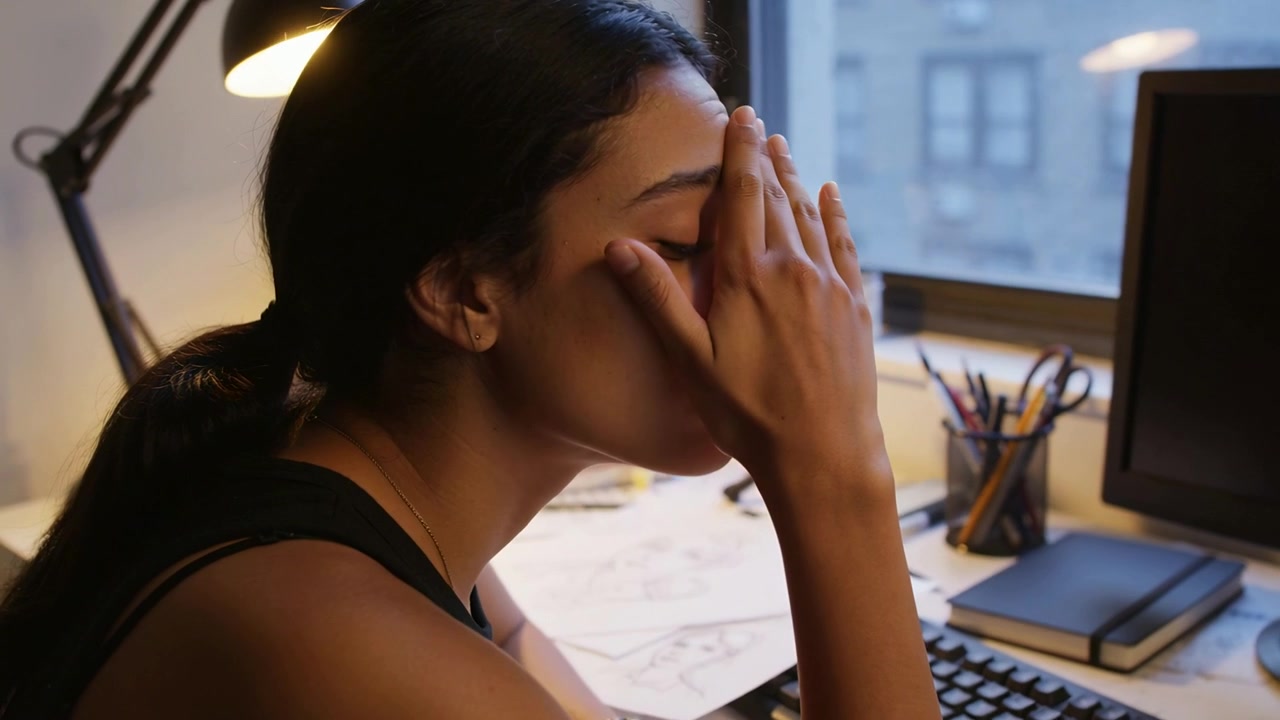Donna con top nero senza maniche che si sfrega gli occhi per alleviare l'affaticamento dopo aver lavorato al computer alla scrivania, con schizzi