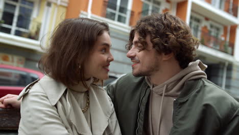 Pareja-Feliz-Coqueteando-Al-Aire-Libre.-Hombre-Y-Mujer-Besándose-En-Un-Banco-En-La-Calle-De-La-Ciudad.