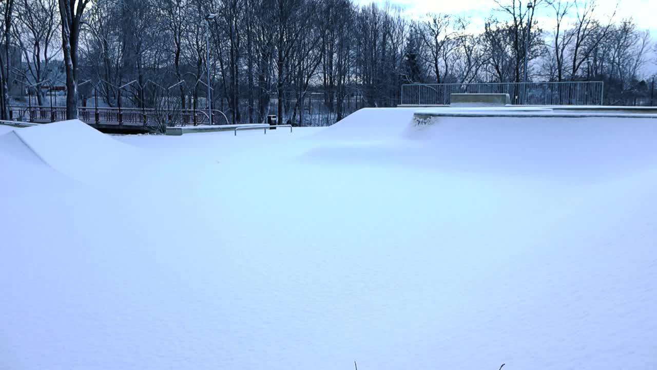 Panning over skatepark blanketed in fresh snow at Laagri, Estonia. Pristine snow covers the entire park landscape. Urban deep snow accumulation. The ramps, rails and concrete structures are under snow