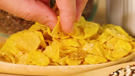 a hand picks cornflakes from a wooden bowl in a well-lit kitchen setting. close-up shots emphasize texture and color