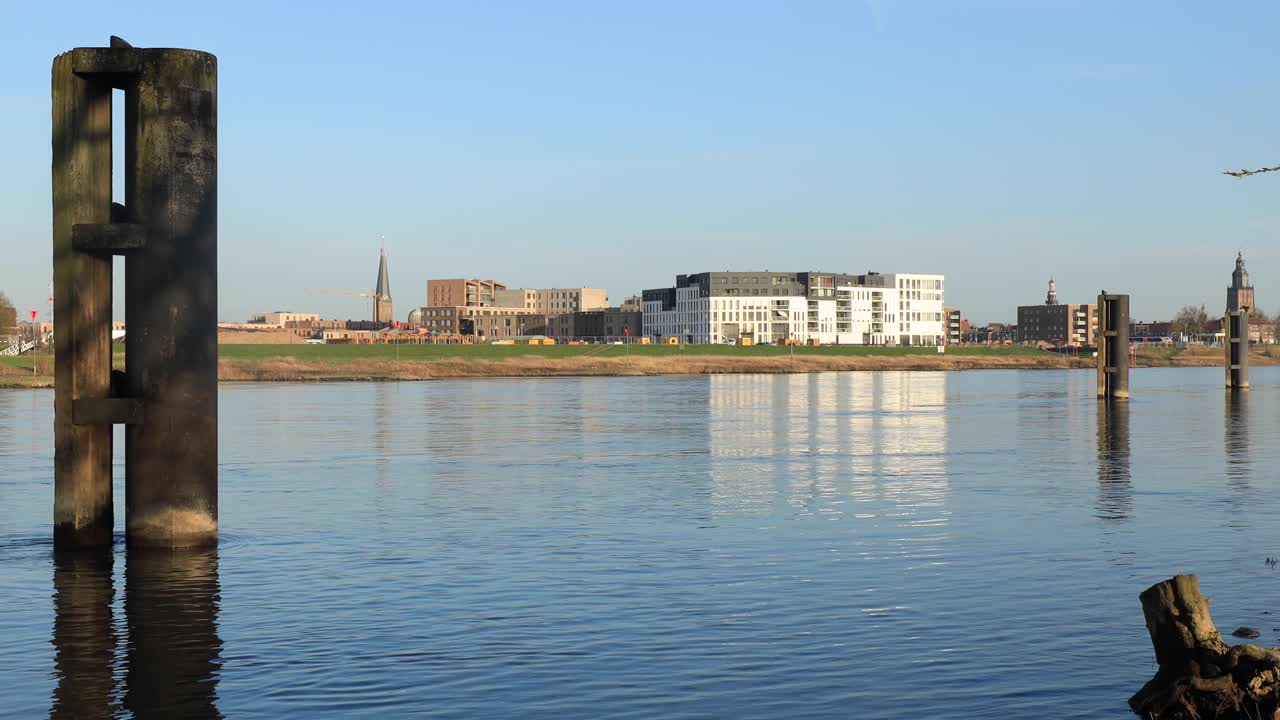 네덜란드 유서 깊은 도시 주펜 인근의 이셀 강을 따라 대형 화물선을 위한 주차장이 있으며, 반대편에는 맑고 푸른 하늘을 배경으로 새로 지어진 고급 아파트 단지가 있습니다.