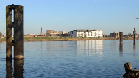 Parking-dock-for-large-cargo-ships-along-the-river-IJssel-near-historic-city-Zutphen,-The-Netherlands,-on-the-other-side-with-newly-build-luxury-apartment-complex-in-front-against-a-clear-blue-sky