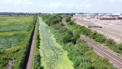 Canal-De-Campo-Cubierto-De-Algas-Verdes-Junto-Con-El-Nuevo-Sitio-De-Construcción-De-Viviendas-Vista-Aérea-Panorámica-Derecha