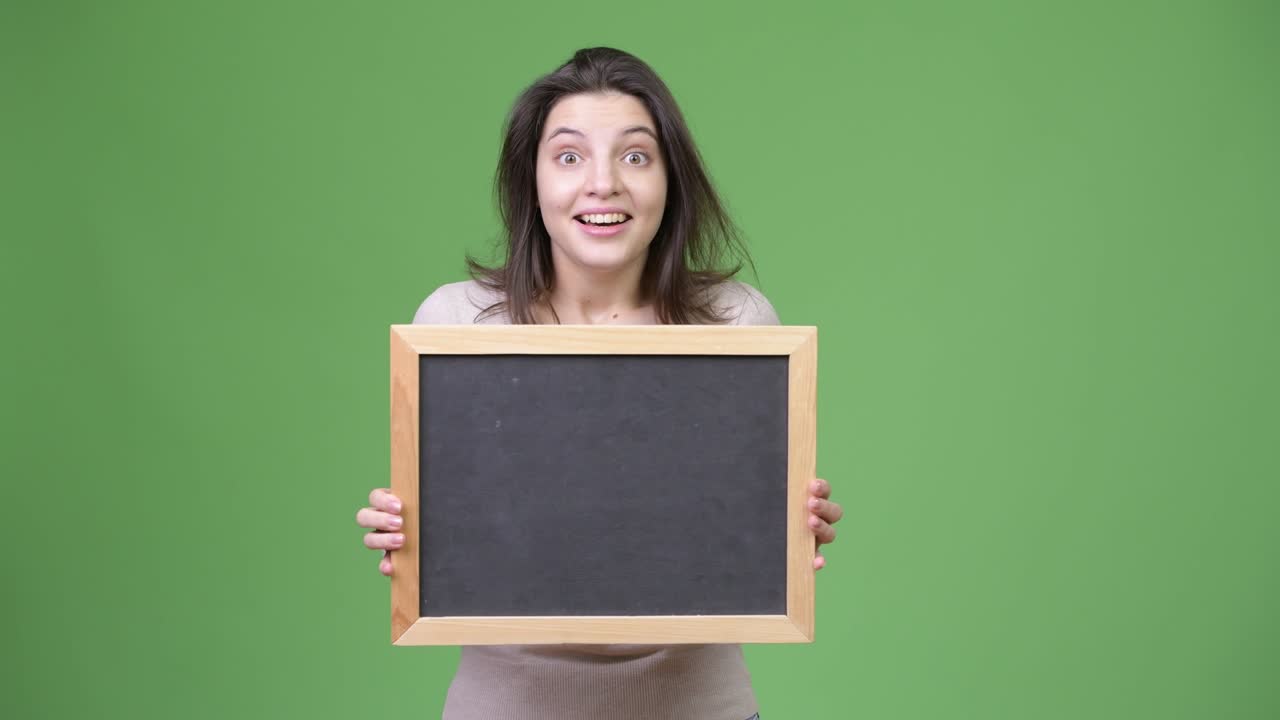 Young beautiful woman looking surprised while holding blackboard